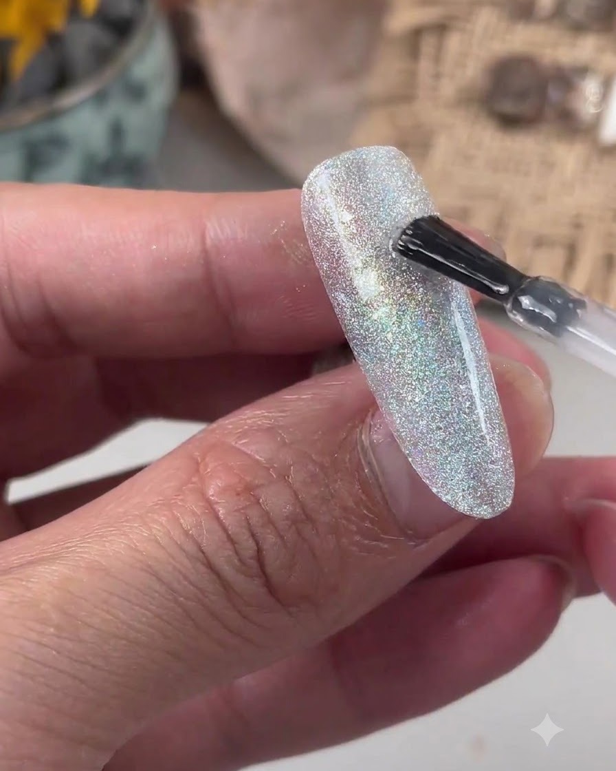 Un pennello che applica il gel livellante trasparente su una superficie ungueale glitterata.