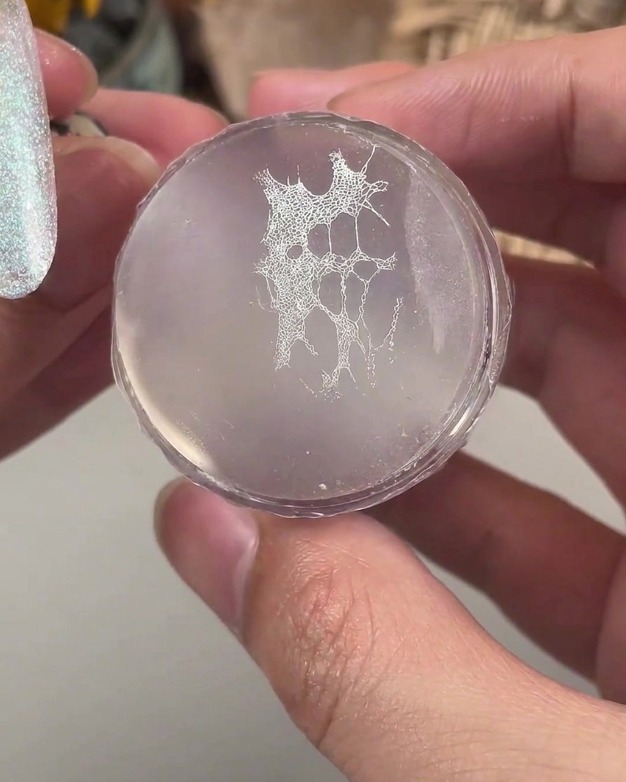 Un timbro in silicone trasparente che sostiene un motivo in pizzo bianco fine pronto per essere trasferito su ununghia manicurata.