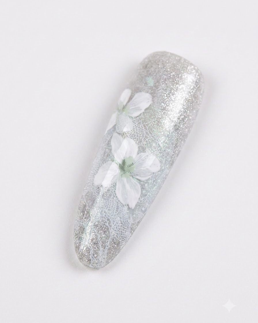 Un primo piano di ununghia manicurata con delicati fiori bianchi con morbida sfumatura grigia su uno sfondo grigio-azzurro brillante.