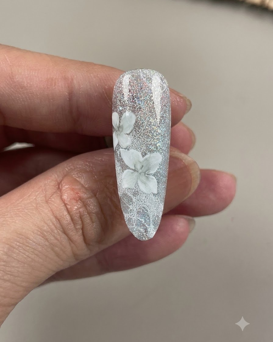 Ununghia completata che mostra dettagliati fiori di camelia bianchi e sfumati su uno sfondo in pizzo grigio-azzurro brillante.