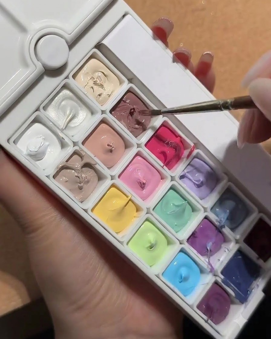 Un pennello per unghie che si intinge in una tavolozza contenente un riquadro di gel nude bianco pesca.