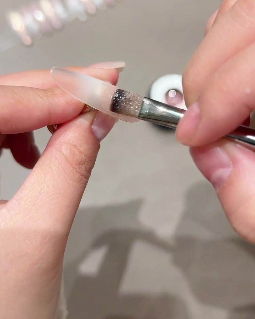 Un pennello che applica il gel cat-eye sulla metà esterna di una tip trasparente.