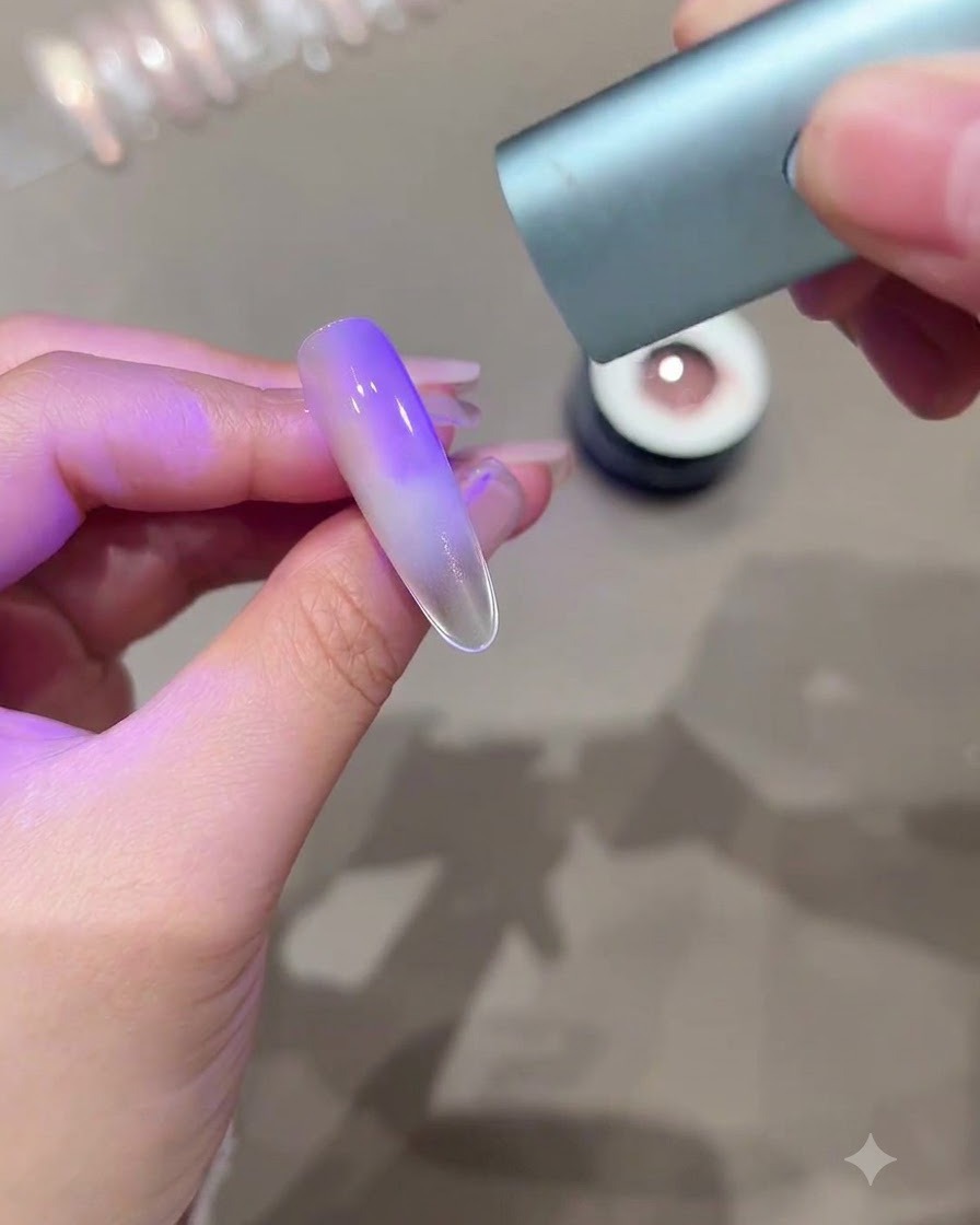 Una mano che regge una mini lampada UV LED sopra ununghia allungata che mostra un effetto cat-eye sfumato viola.