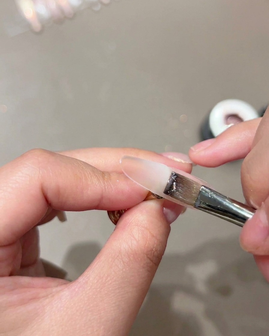 Un pennello piatto che applica uno strato base nude trasparente su un supporto per unghie.