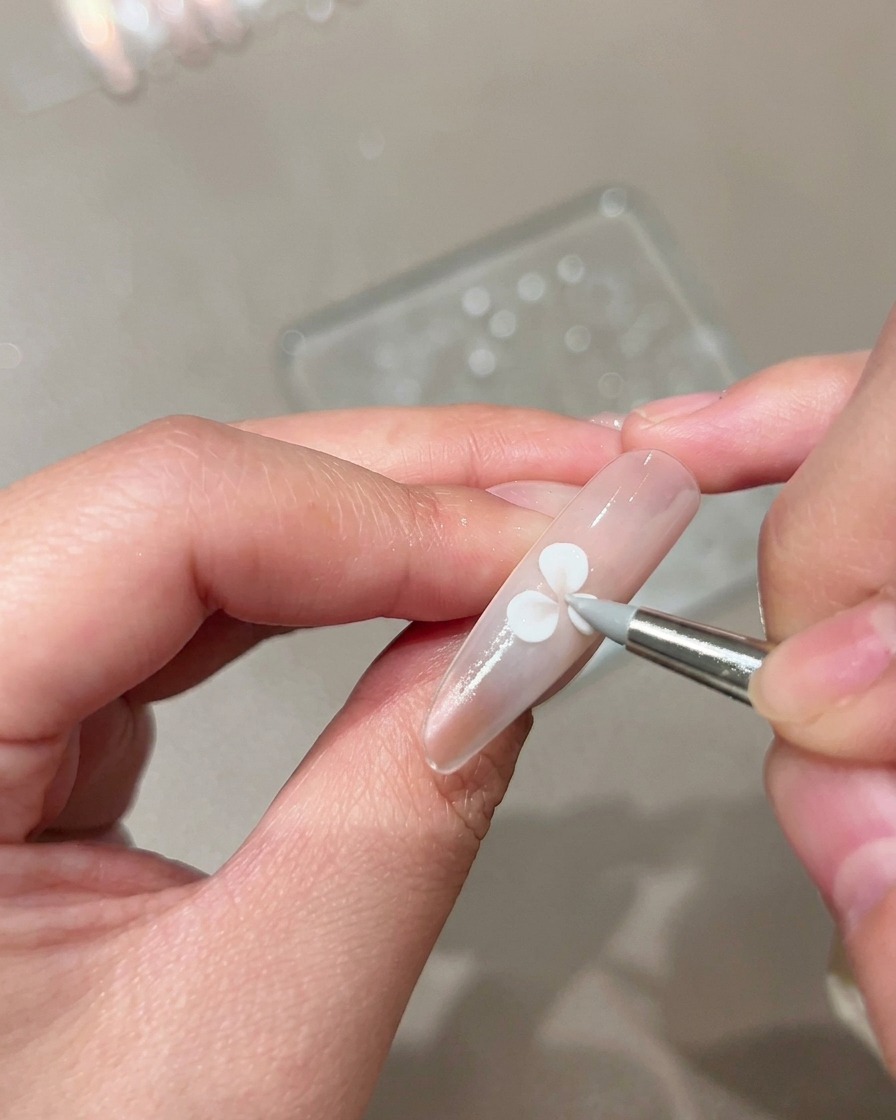 Un pennello da scultura in silicone che preme e modella un petalo in gel bianco su ununghia nude curata.