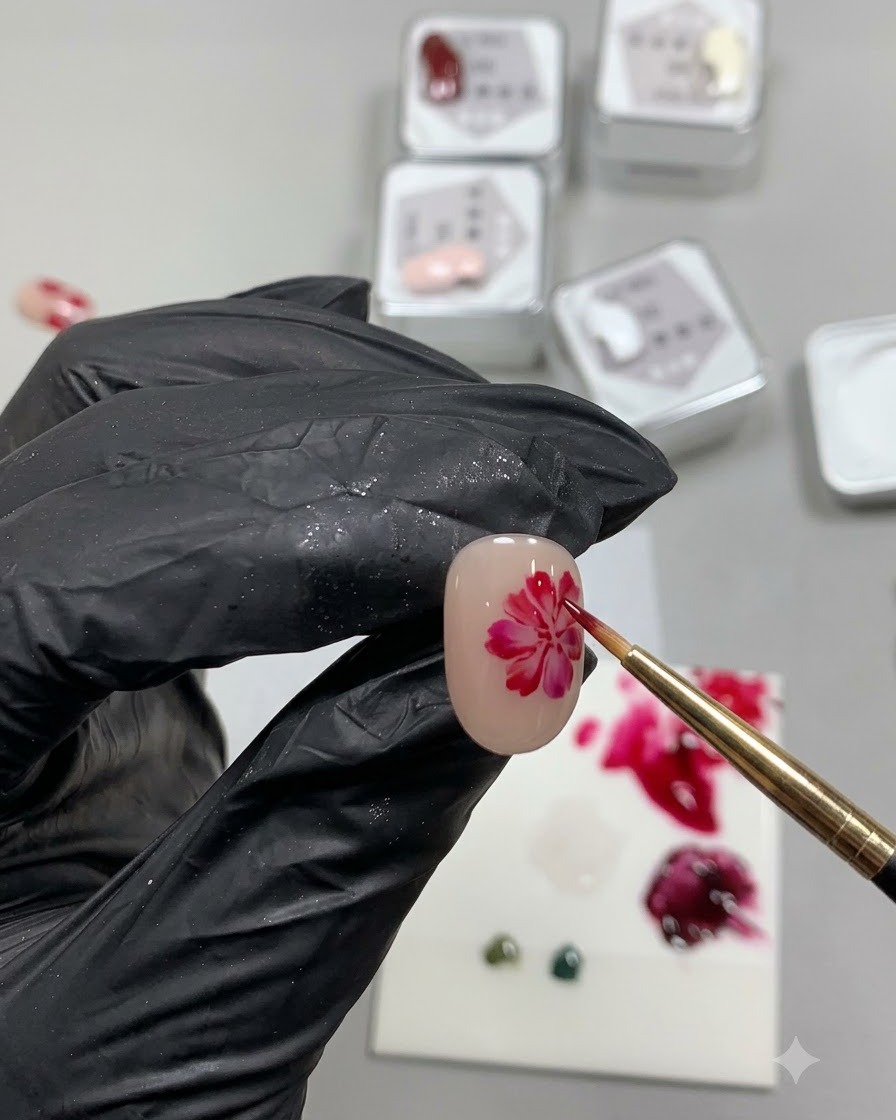 Un pennello fine per dettagli che dipinge un cerchio rosso morbido, traslucido e irregolare che ricorda la base di un petalo di rosa su ununghia nude.