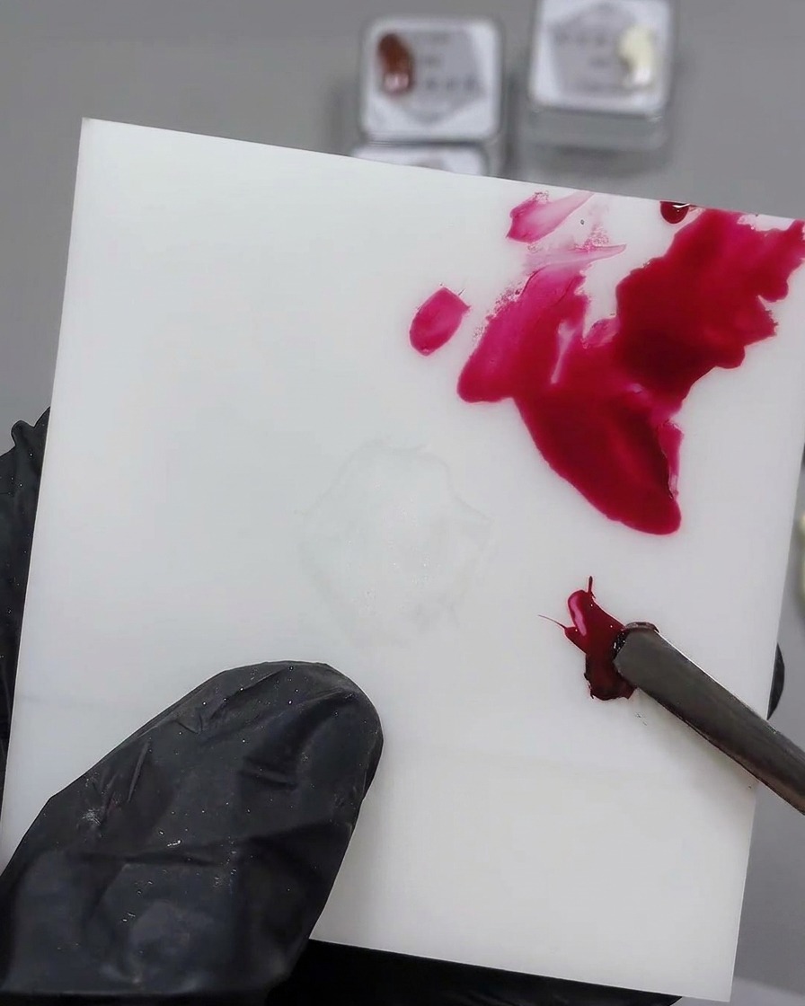 Uno strumento metallico che mescola il gel nero in una goccia di gel rosso su una tavolozza bianca.