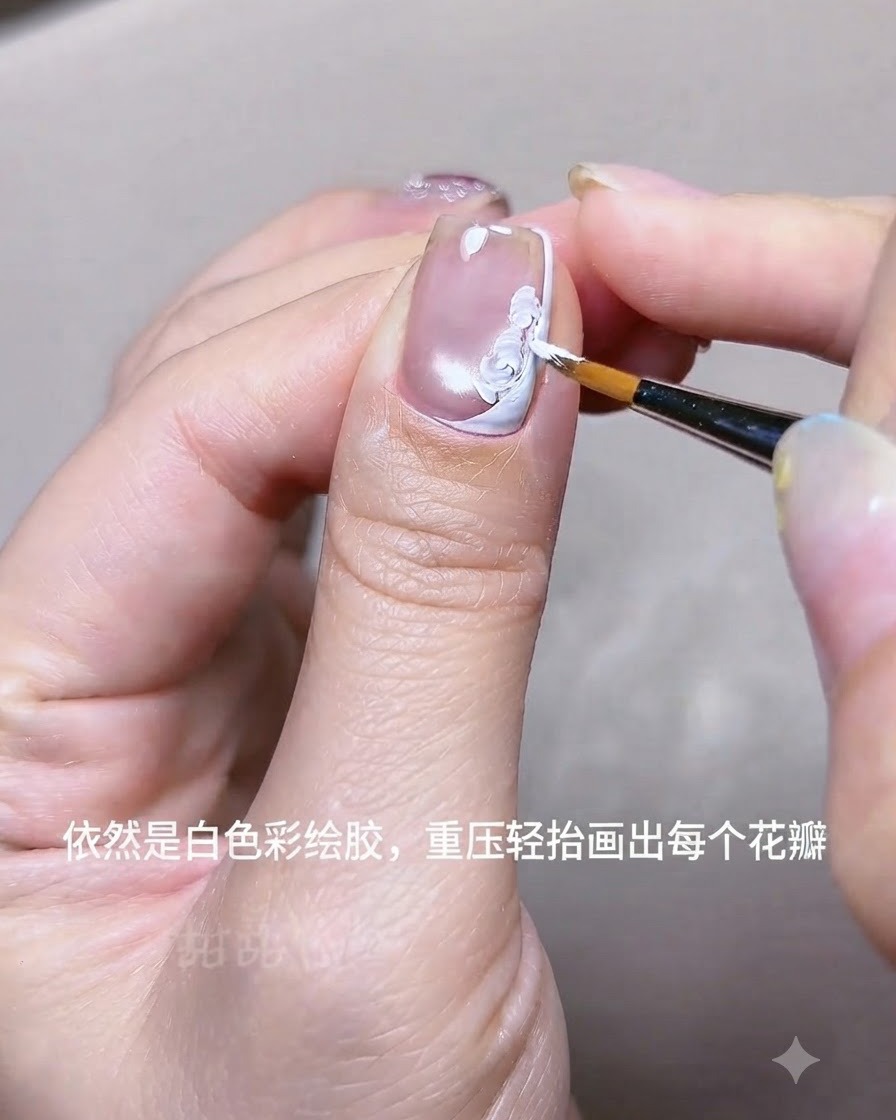 Una vista ravvicinata di una mano che utilizza un pennello liner fine per dipingere petali di fiori in gel acrilico bianco su ununghia vicino a una linea French bianca.