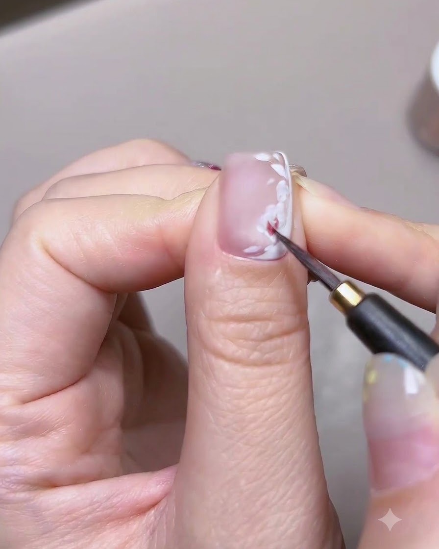 Un primo piano dettagliato di un pennello fine che applica vernice ad acquerello rossa sulla base dei petali bianchi di una nail art a rosa.