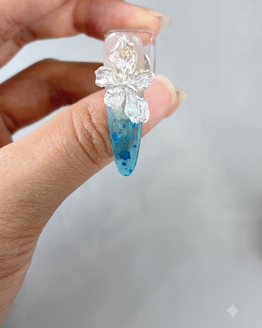 Una pinzetta che posiziona una piccola perla bianca al centro di un fiore 3D scolpito su ununghia.