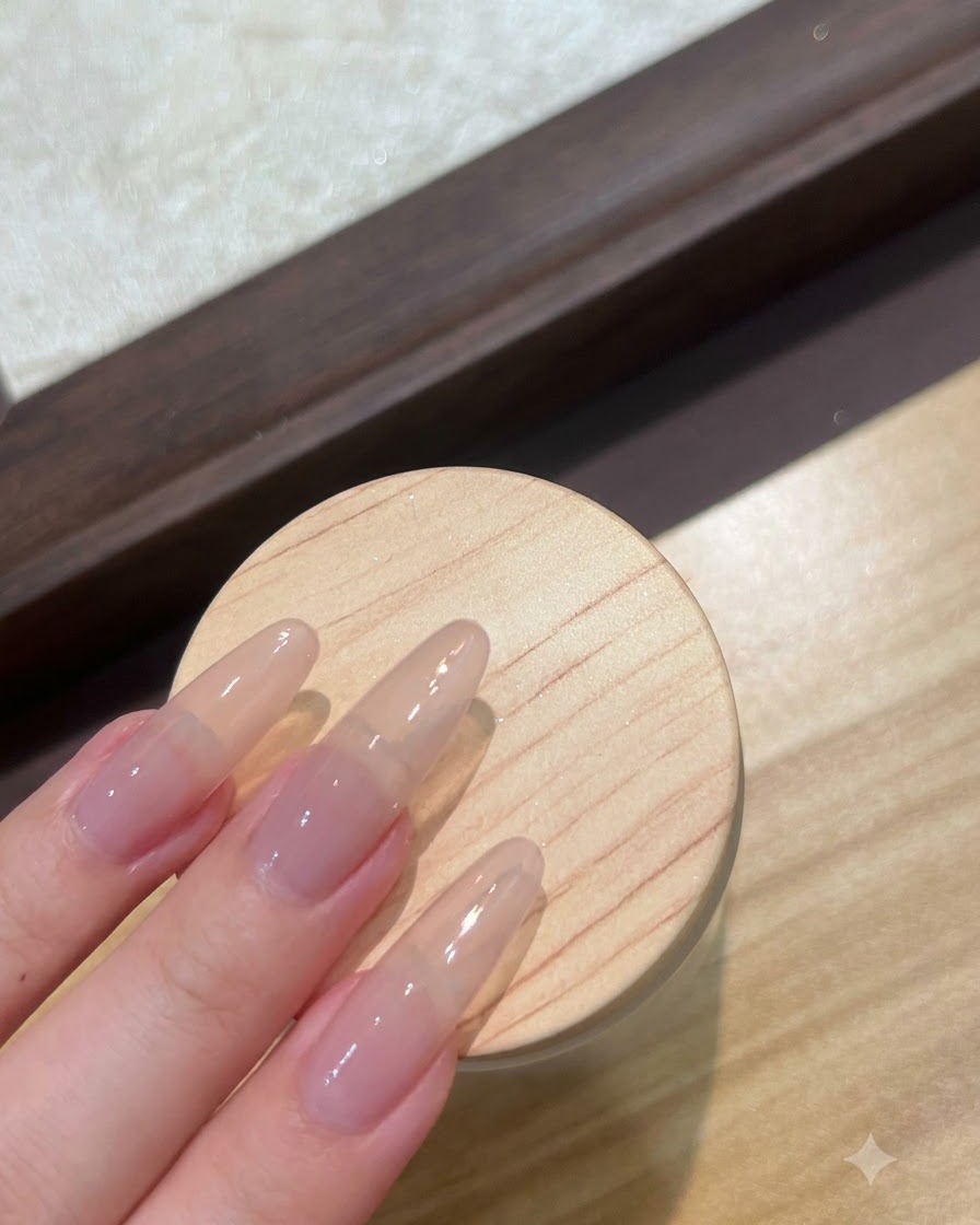 Una vista ravvicinata di unghie lunghe con extension nude preparate con uno strato di gel base trasparente.