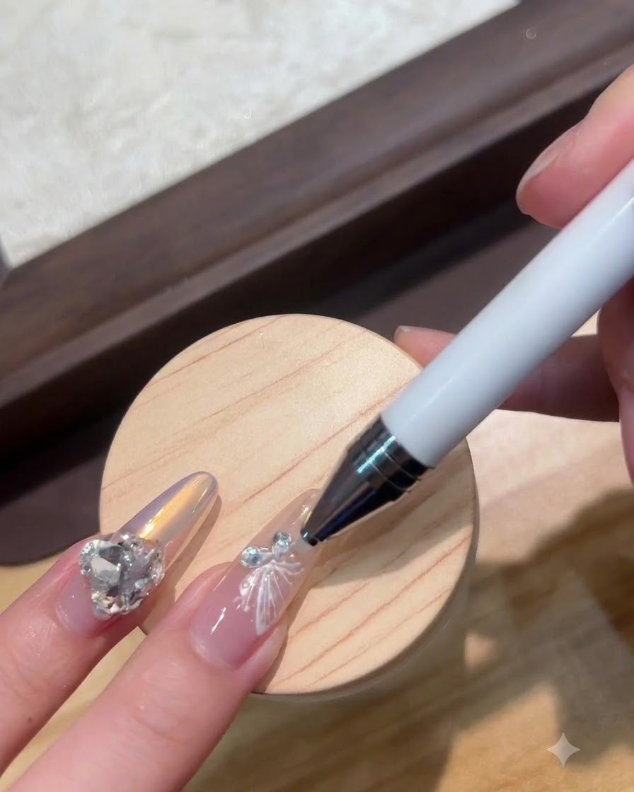 Una penna dotting posiziona un minuscolo cristallo accanto a un charm per unghie a farfalla bianca.