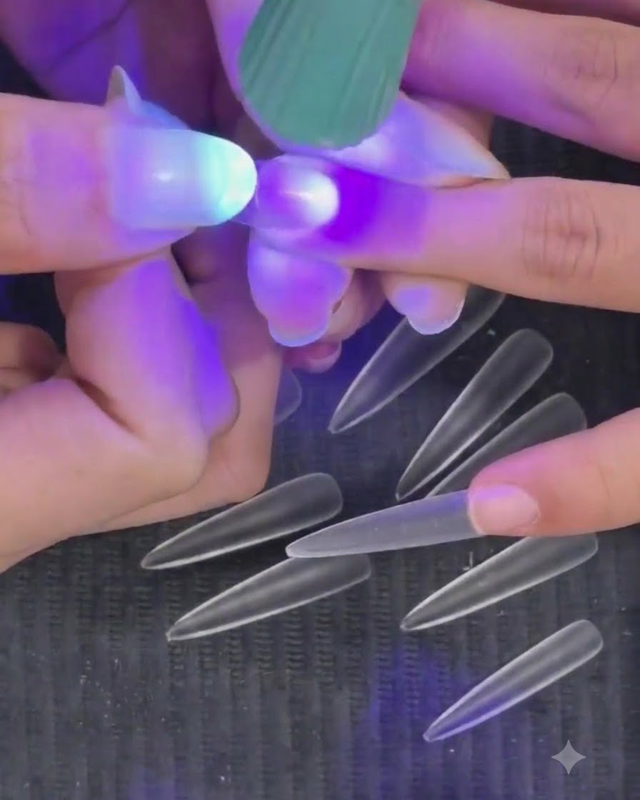 Una mano che tiene una mini torcia LED UV viola sopra ununghia per polimerizzare una tip semi-polimerizzata.