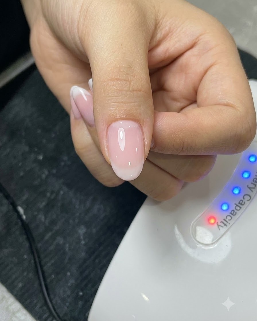 Un pennello che applica uno strato di top coat su ununghia curata davanti a una lampada UV.