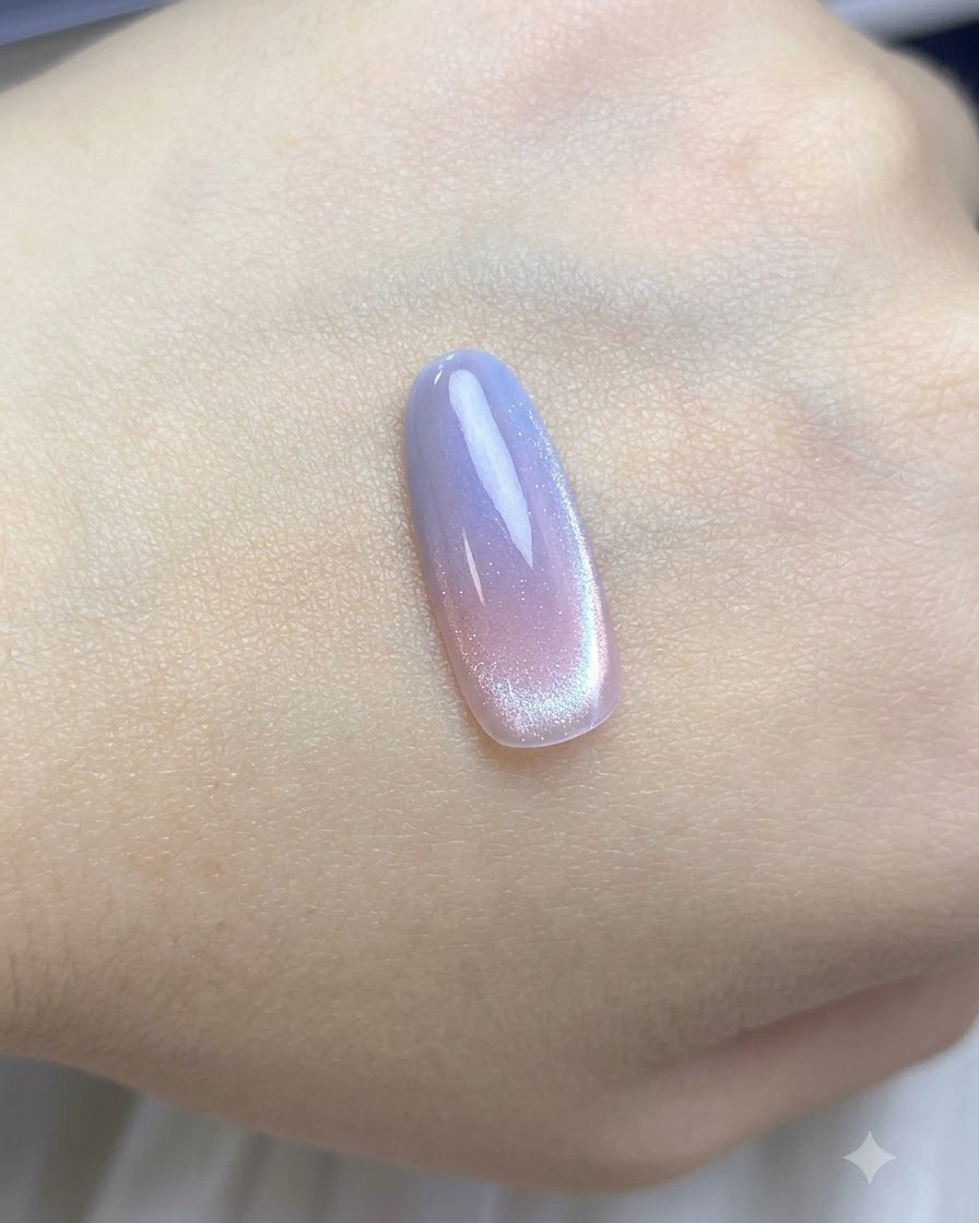 Un pennello che stende una mano di smalto cat-eye nude trasparente sul tip sfumato.