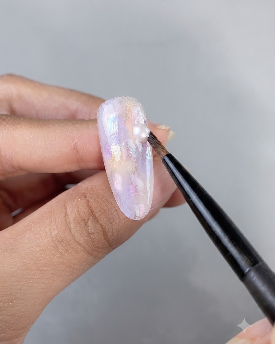 Un pennello liner fine che applica una goccia di gel brillante su una superficie dunghia decorata con conchiglie.