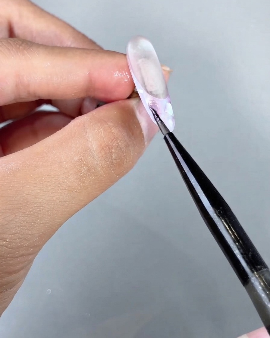 Un pennello fine che applica il magico gel cat eye sea su una sezione specifica di un design per unghie texturizzato.