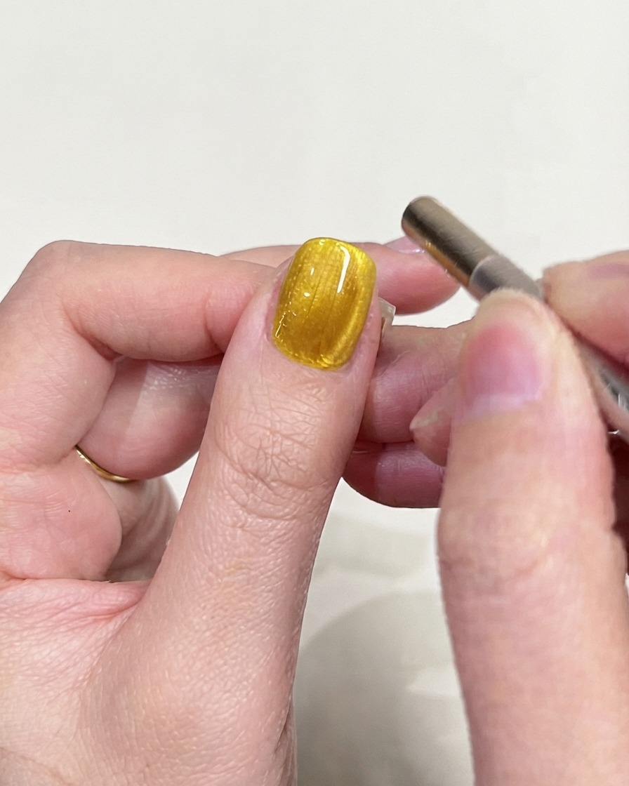Scatto di ispezione dettagliato di ununghia in gel cat-eye giallo incentrato sul riflesso della luce magnetica.