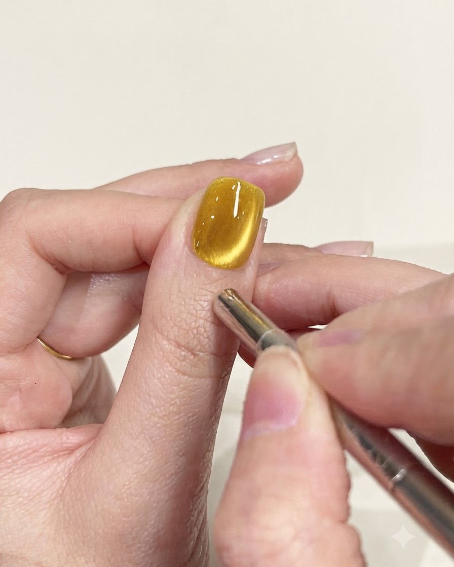 Uno strumento a penna magnetica di precisione utilizzato per perfezionare il percorso del riflesso su ununghia cat-eye gialla.