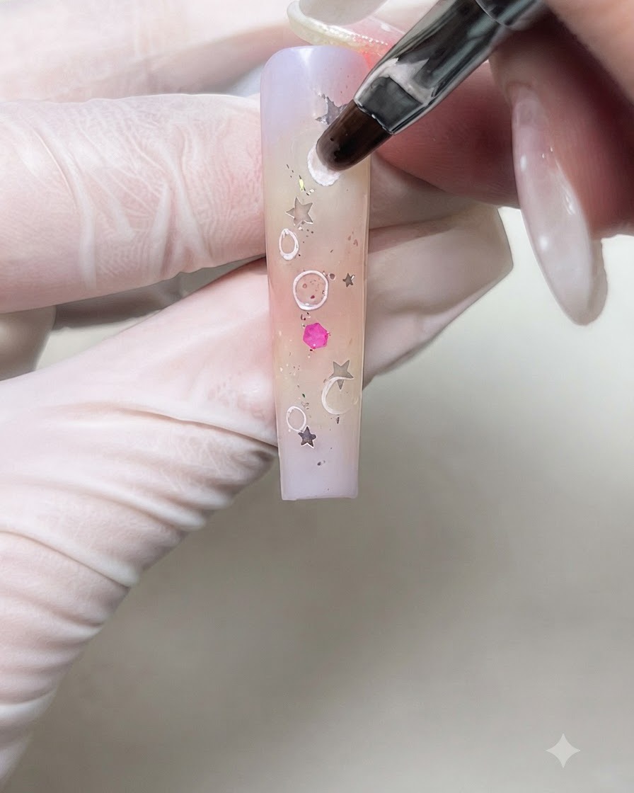 Un pennello per nail art che sfuma dolcemente i bordi interni dei cerchi di crema bianca su ununghia sfumata.