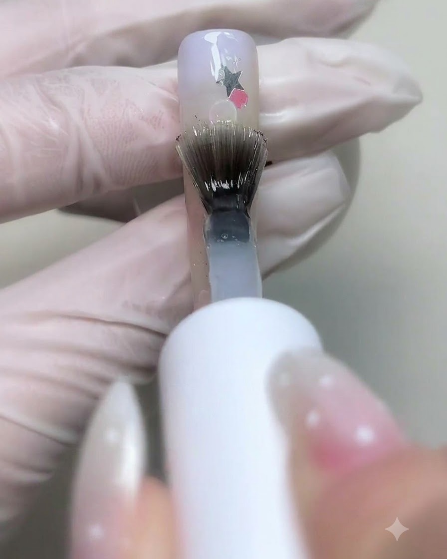 Un pennello che applica il base gel trasparente sulle unghie decorate con paillettes a stella e bolle.