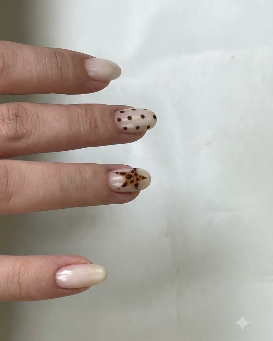 Un pennello applica il top coat trasparente su ununghia con pois marroni e un design a stella.