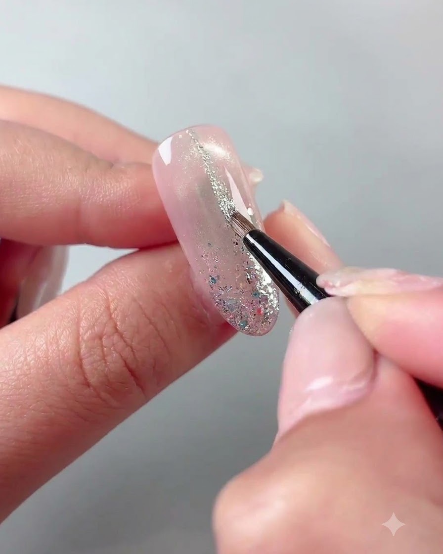 Un pennello sottile da liner che disegna sottili linee di glitter argento su una superficie di unghia polimerizzata.
