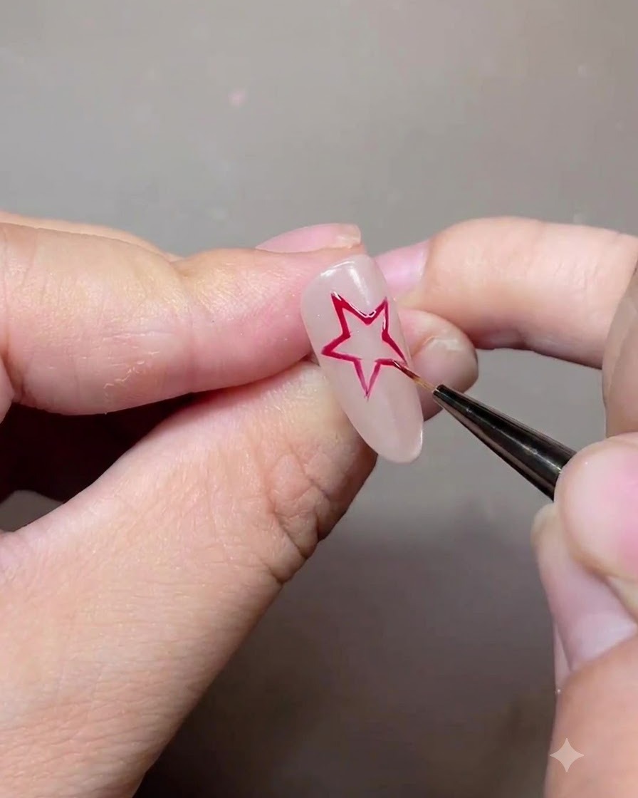 Un pennello sottile che disegna il contorno di una stella a cinque punte rossa su ununghia in gel nude.