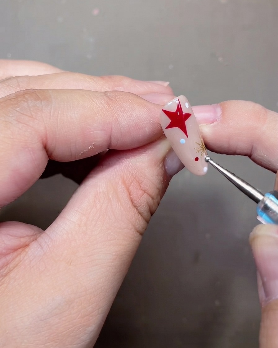 Uno strumento per puntinatura che posiziona minuscoli pois bianchi e rossi su ununghia in gel nude decorata.