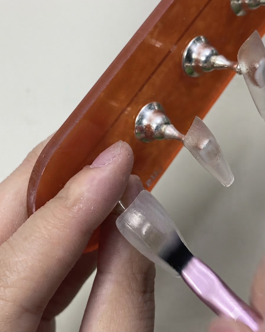 Un pennello che applica con cura la mano iniziale di smalto semipermanente bianco latte velato su una tip da练习.