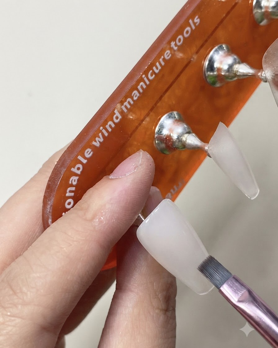 Un pennello che applica uno strato di top coat lucido sullextension unghia in bianco latte polimerizzato.