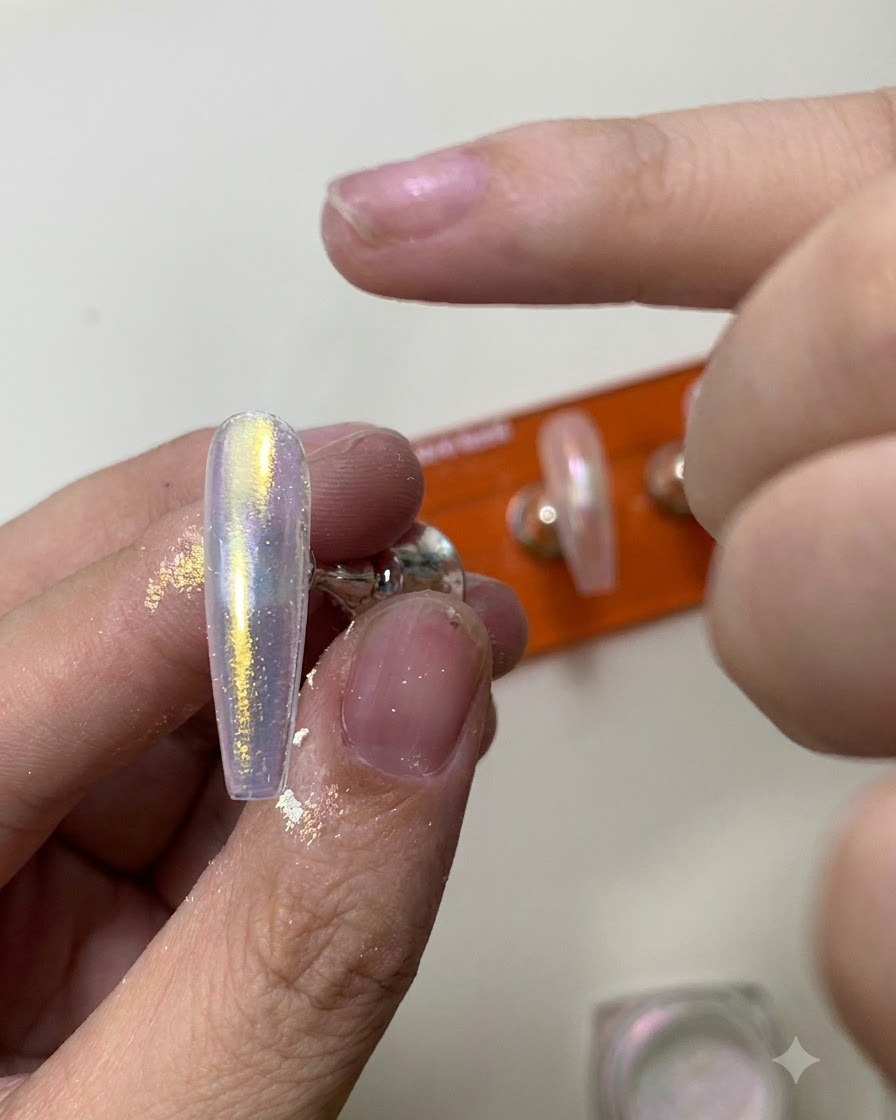 Uno strumento in silicone che sfrega la polvere cromata aurora brillante su una superficie ungueale lucida.