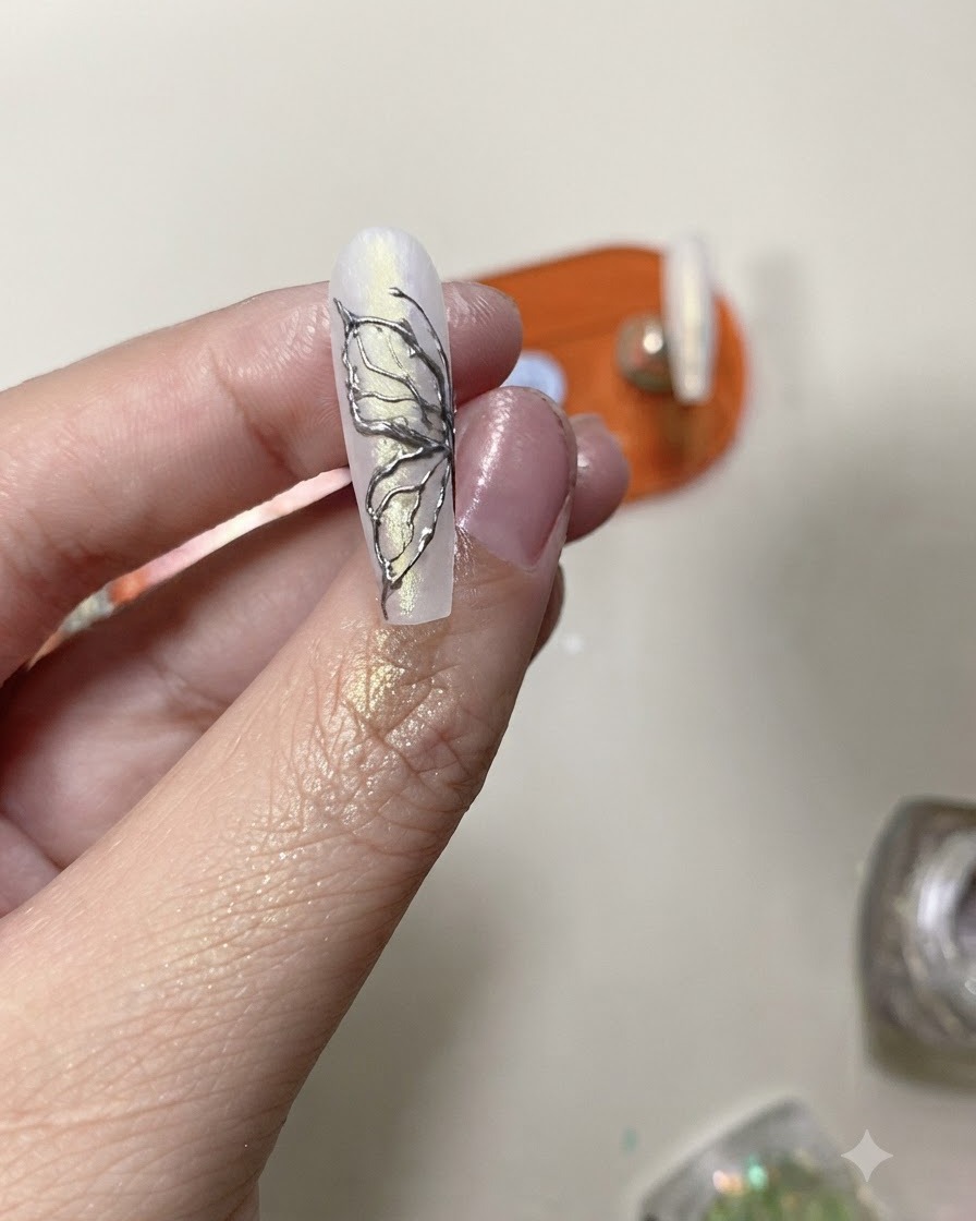 Un pennello per top coat che applica uno strato protettivo trasparente su un design di unghie a farfalla in cromo argento finito.