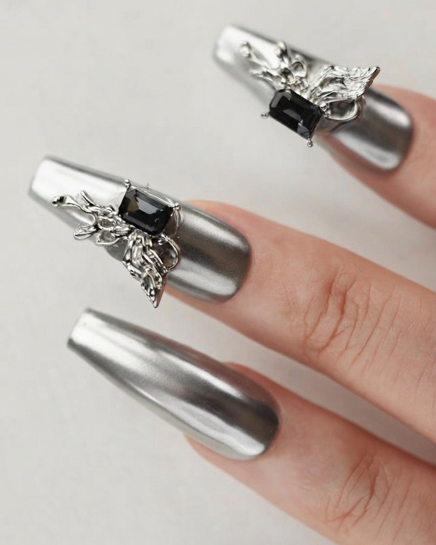 Primo piano di un dito che mostra ununghia cromo argento decorata con un charm farfalla 3D dettagliato e un cristallo scuro.