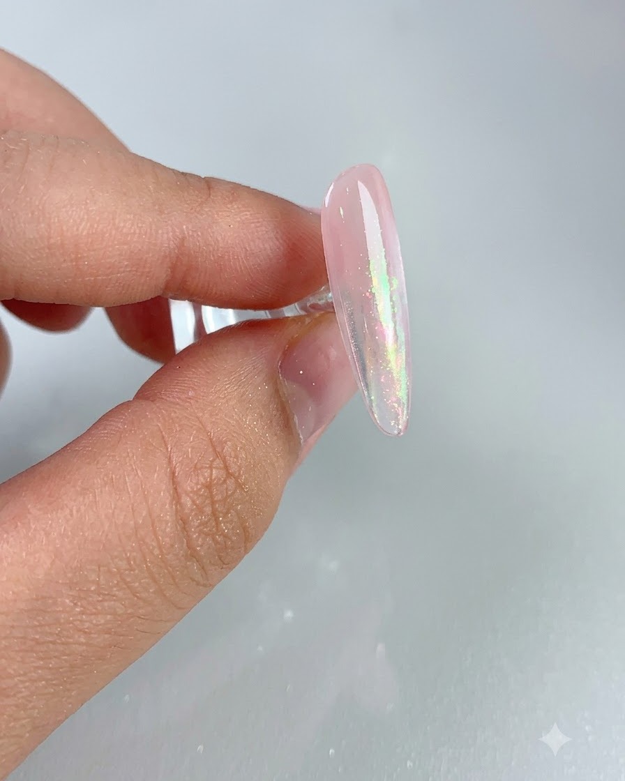 Primo piano di ununghia rosa lucida che mostra un effetto aurora brillante dopo aver spazzolato via la polvere in eccesso.