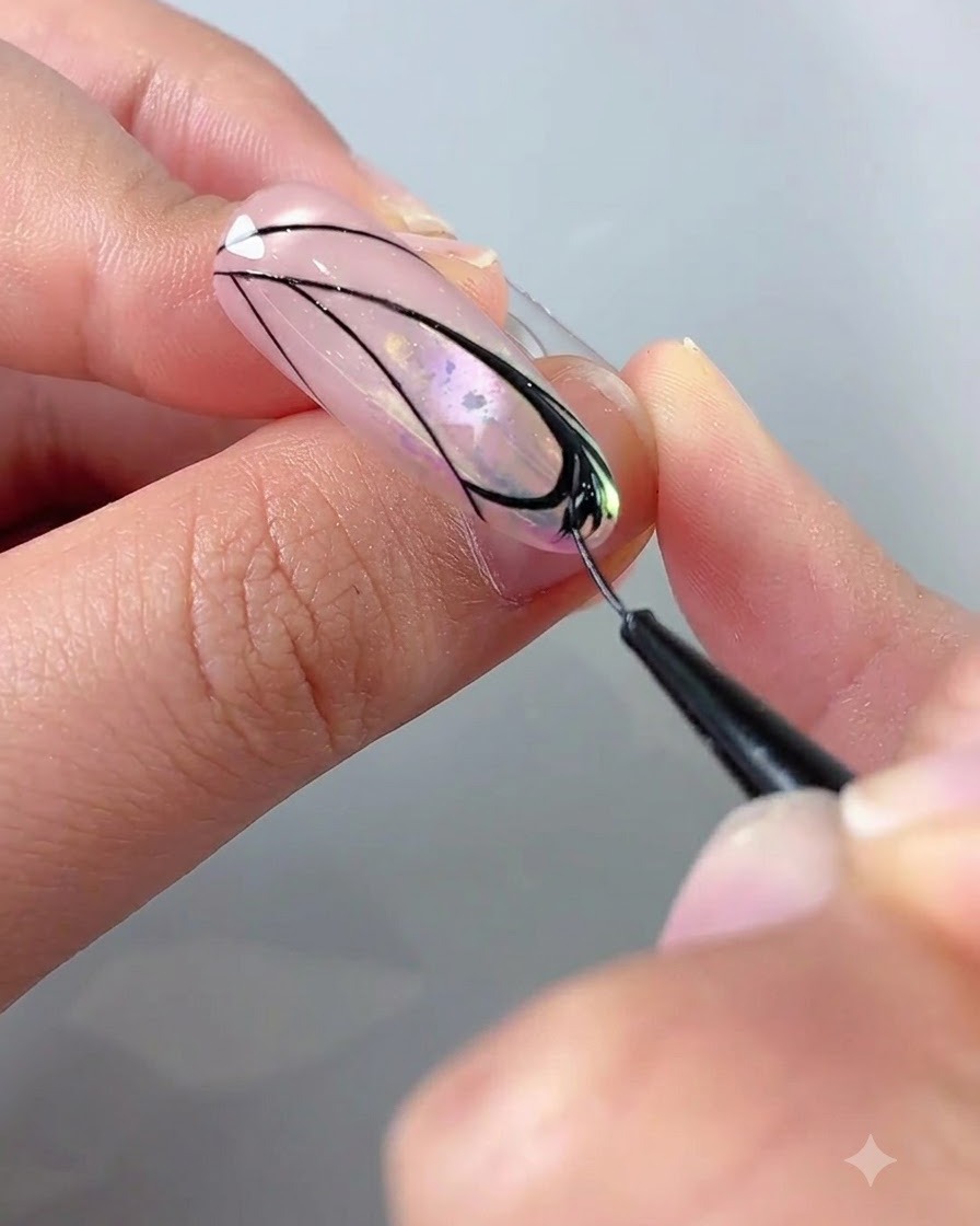 Primo piano di una mano che utilizza un pennello liner con gel nero per riempire i dettagli allinterno di un design ad ala di farfalla su ununghia.