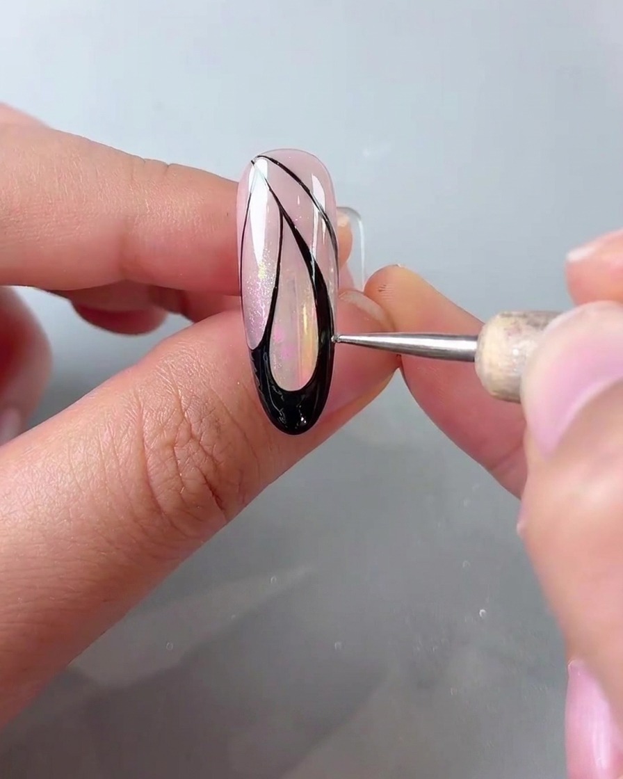 Un dotting pen che posiziona piccoli punti bianchi lungo il margine esterno della nail art nera con ali di farfalla.