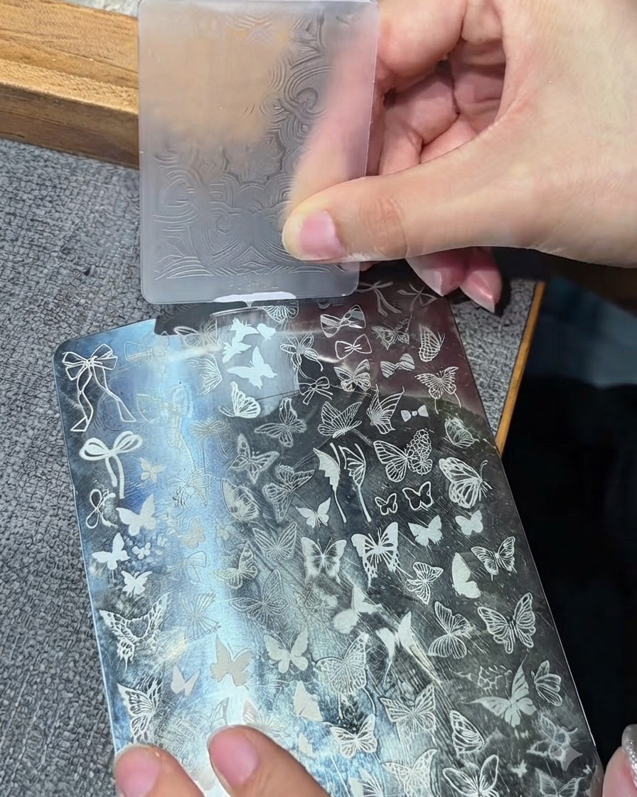 La testa di un timbro in silicone trasparente che preme su un disco da stamping in metallo per raccogliere un disegno bianco.