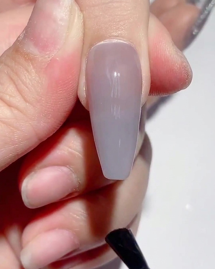 Un pennello che applica il top coat opaco sulla superficie di ununghia dipinta.