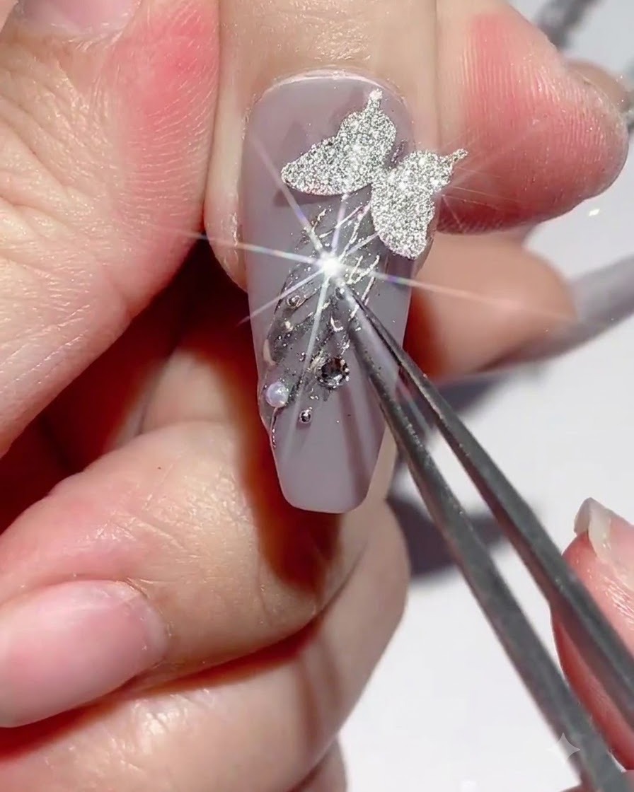 Un paio di pinzette che tengono un ciondolo mentre viene applicata la colla per strass attorno alle decorazioni dellunghia.