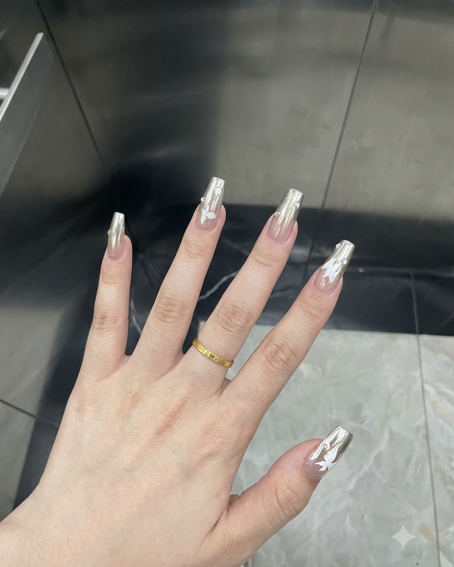 Primo piano dettagliato di un dito che mostra una decalcomania a farfalla bianca applicata su ununghia chrome argento.