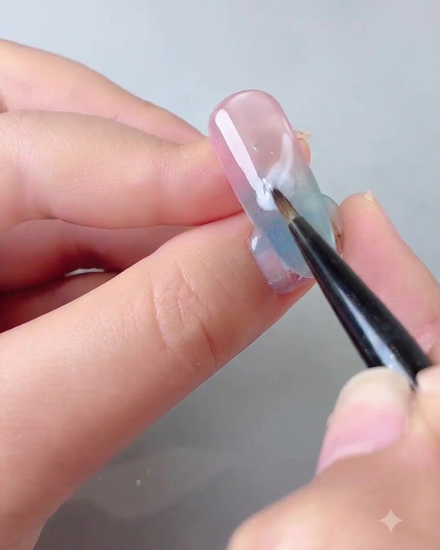 Un pennello a punta fine che applica un gel autolivellante bianco latte in una morbida forma di nuvola su ununghia sfumata.