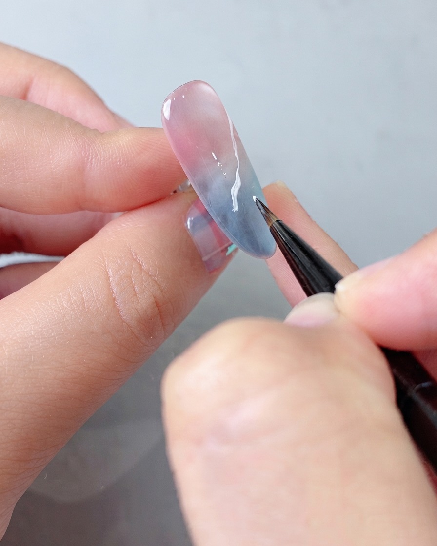 Un pennello per dettagli che applica un ulteriore strato di gel bianco sul motivo a nuvola per una maggiore profondità.