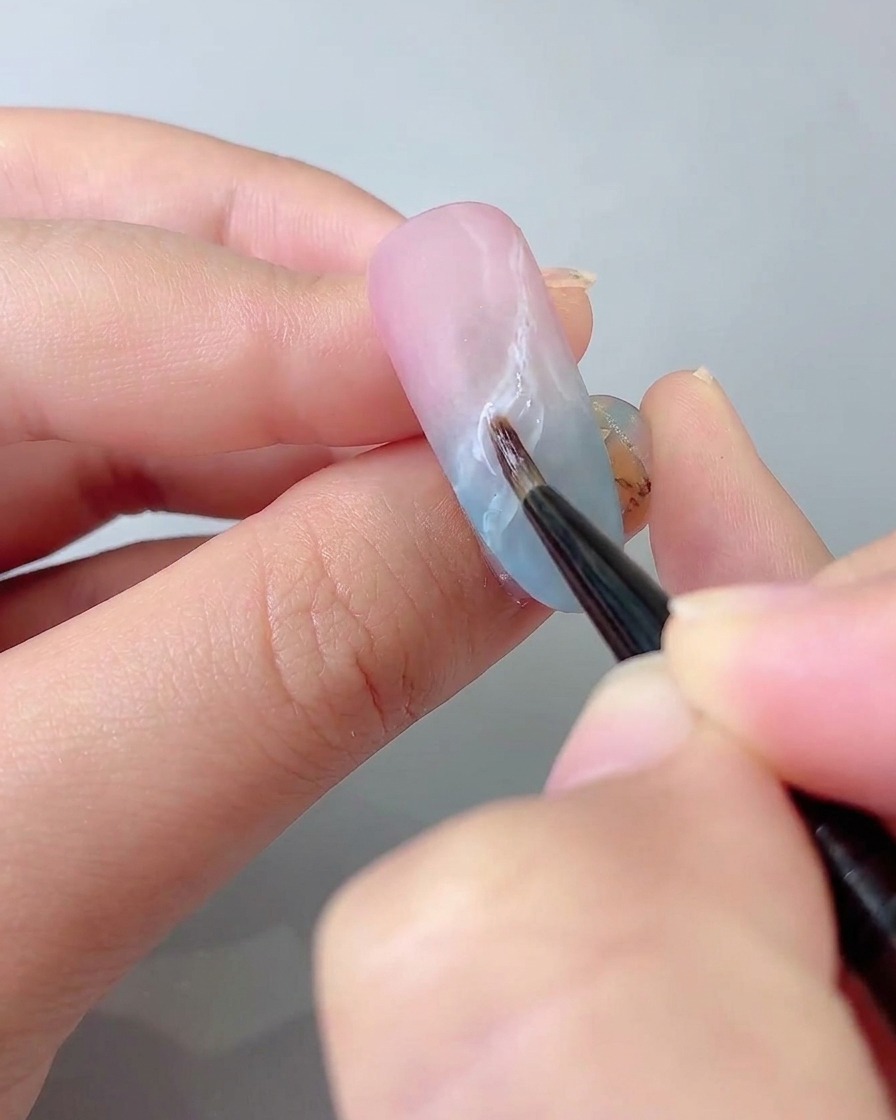 Un pennello di dettaglio fine che disegna delicate linee a nastro sulla superficie dellunghia con colla per gemme appiccicosa.