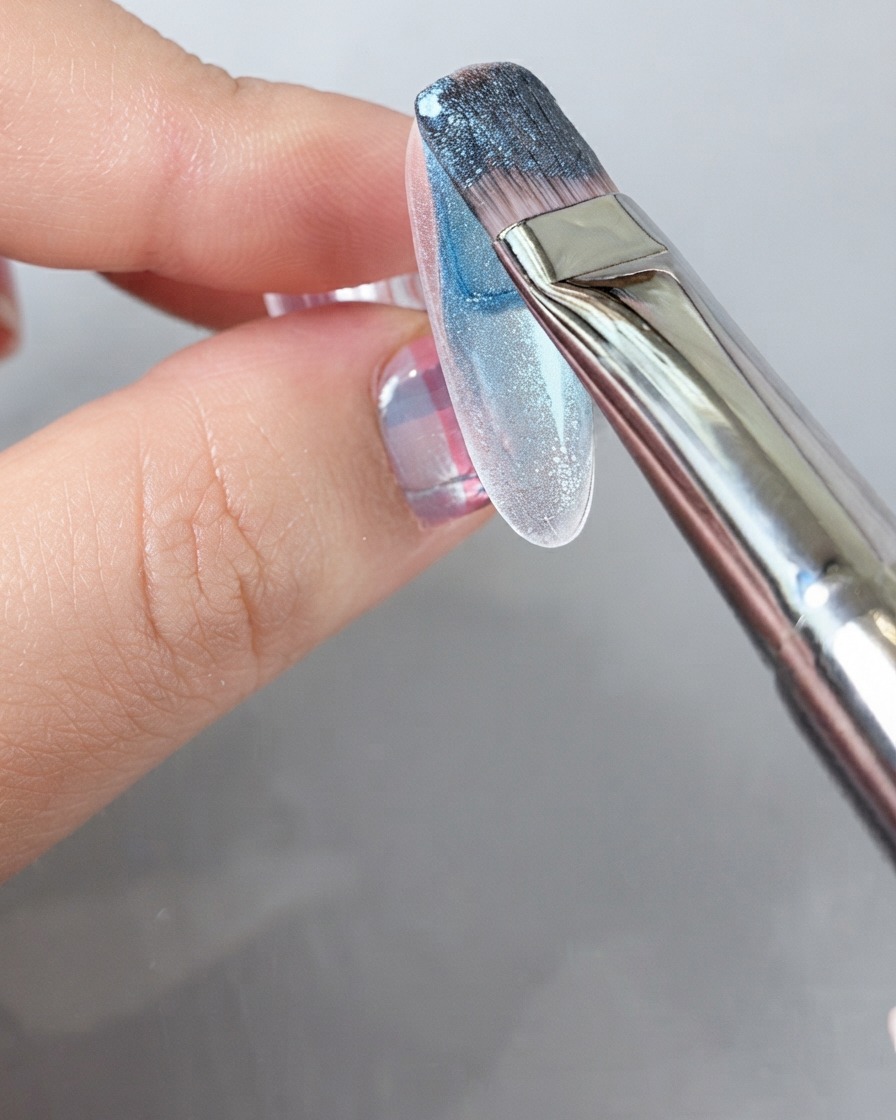 Un pennello che applica un ricco gel polish blu su tutta la superficie di ununghia.