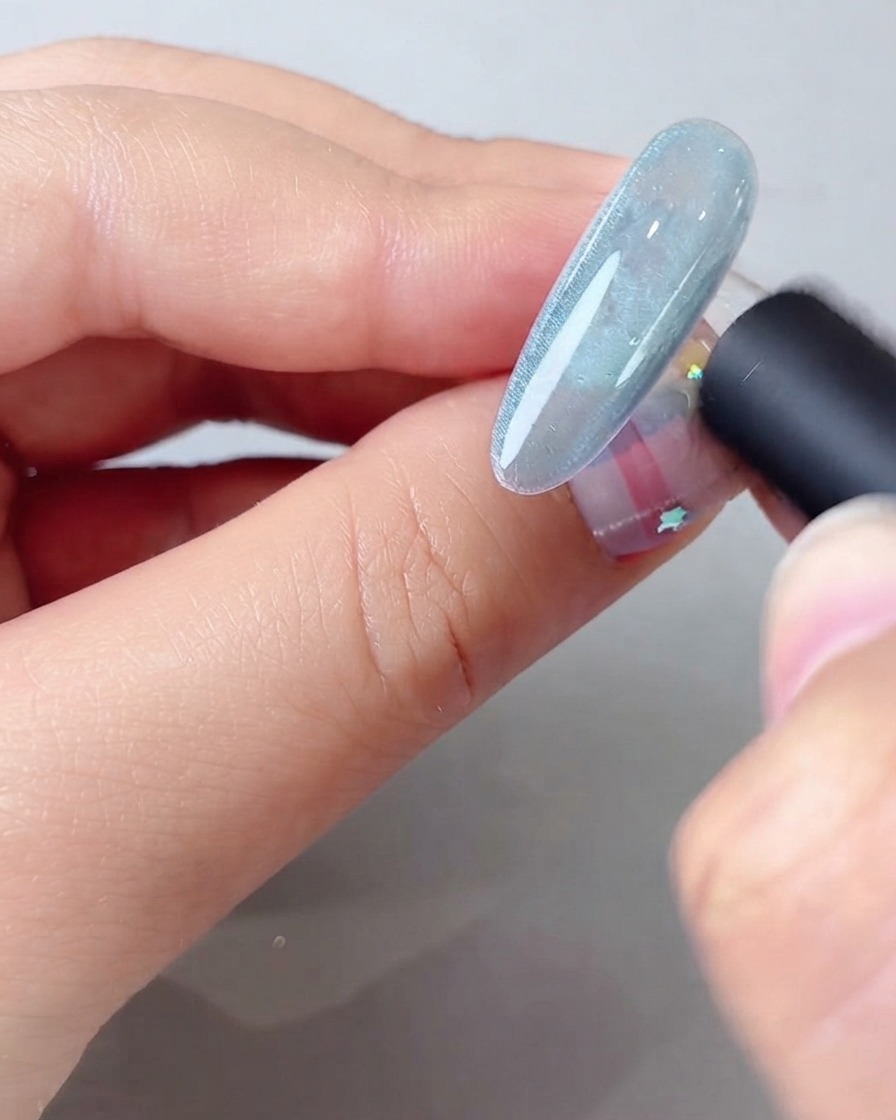 Uno strumento magnetico tenuto vicino a unghie in gel cat eye blu per formare un ampio raggio di luce brillante.
