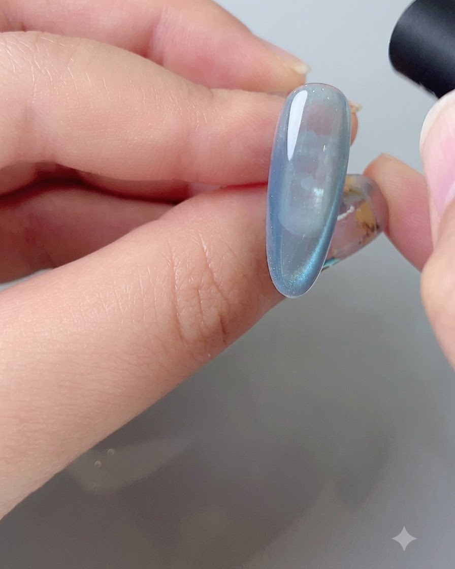 Uno strumento magnetico che modella larco di riflessione laterale su unghia in gel cat eye blu.