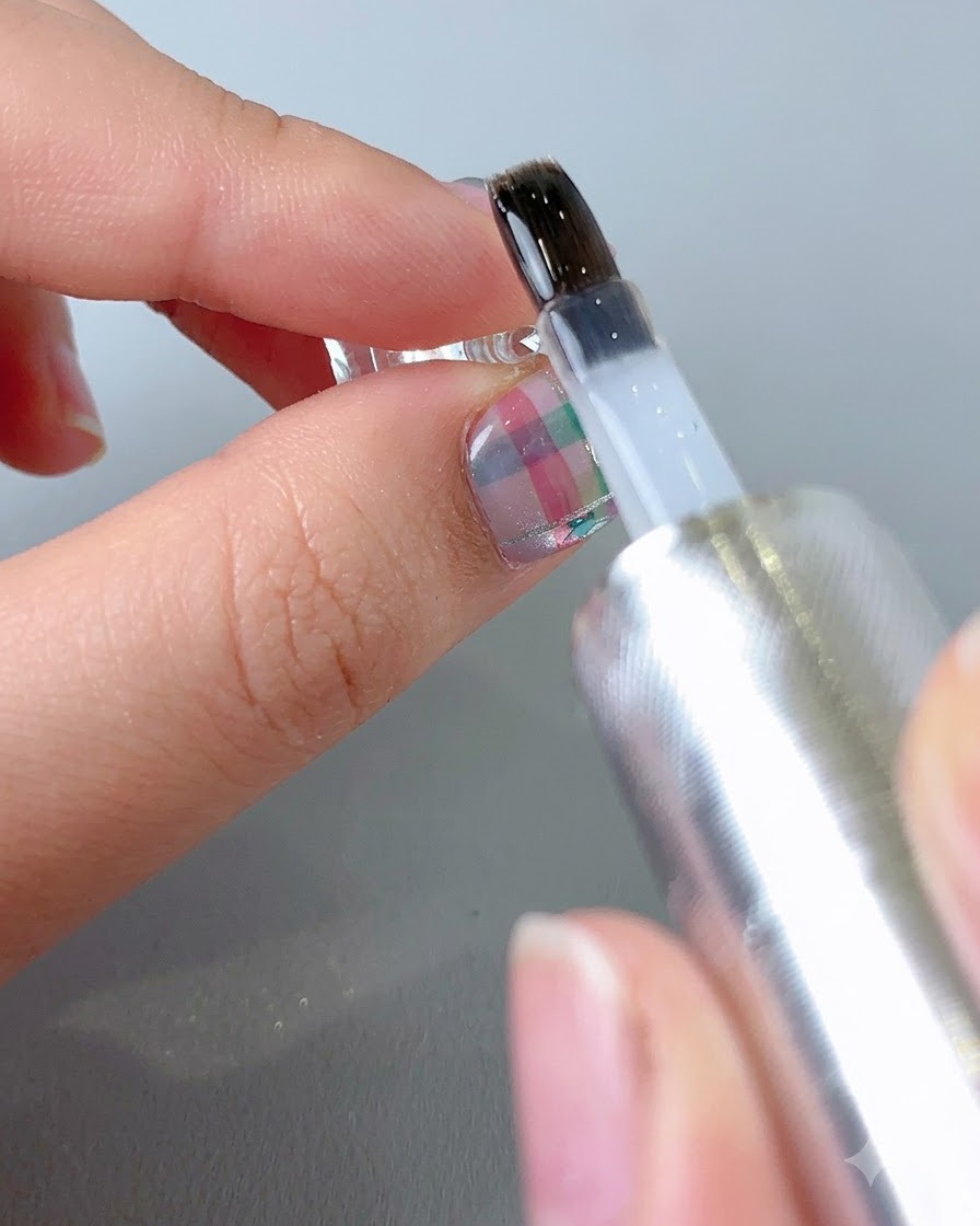 Un pennello che applica un top coat trasparente e lucido sulla superficie di ununghia decorata finita.