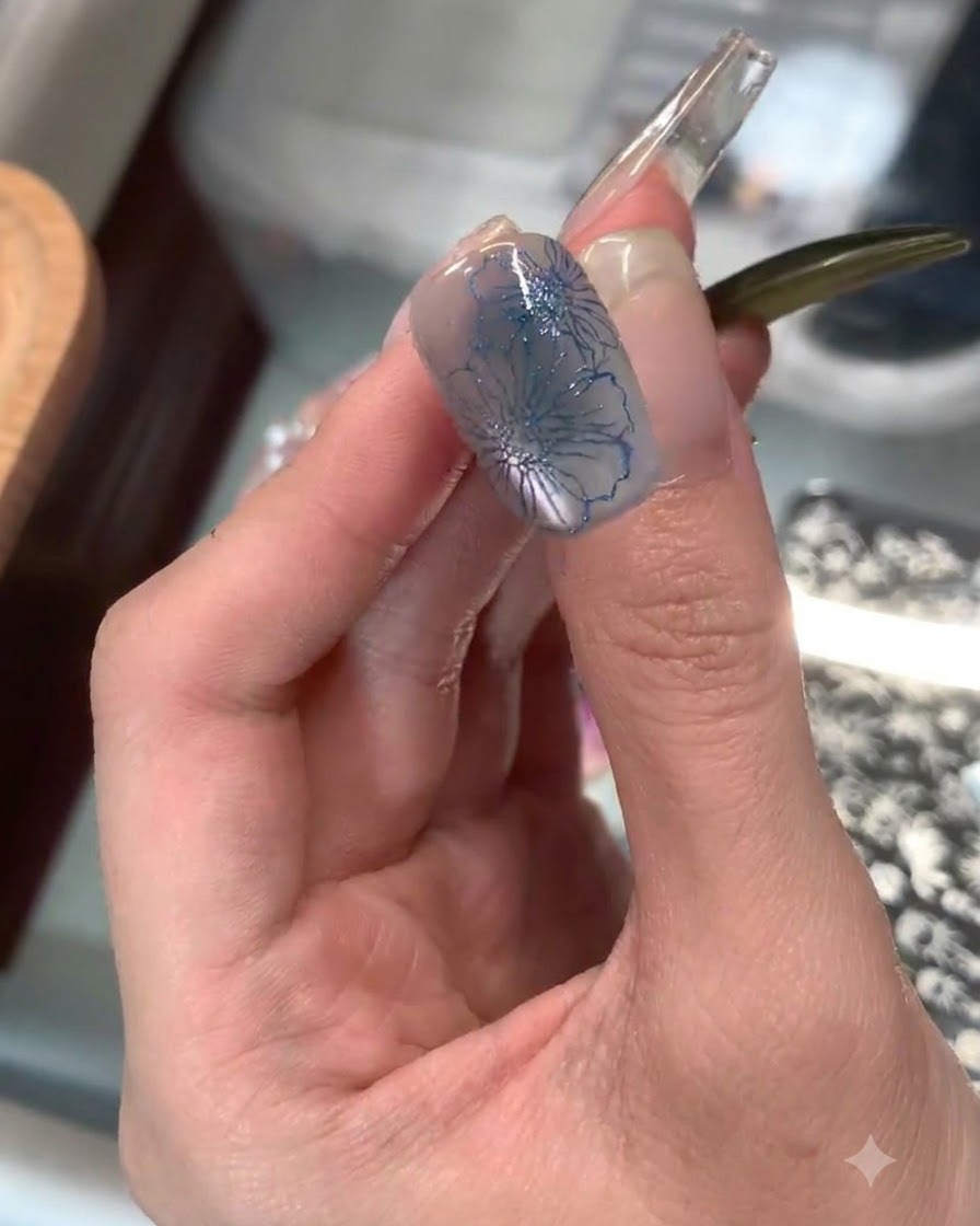 Un timbro in silicone trasparente che applica una delicata stampa floreale blu sulla punta di un dito indice.