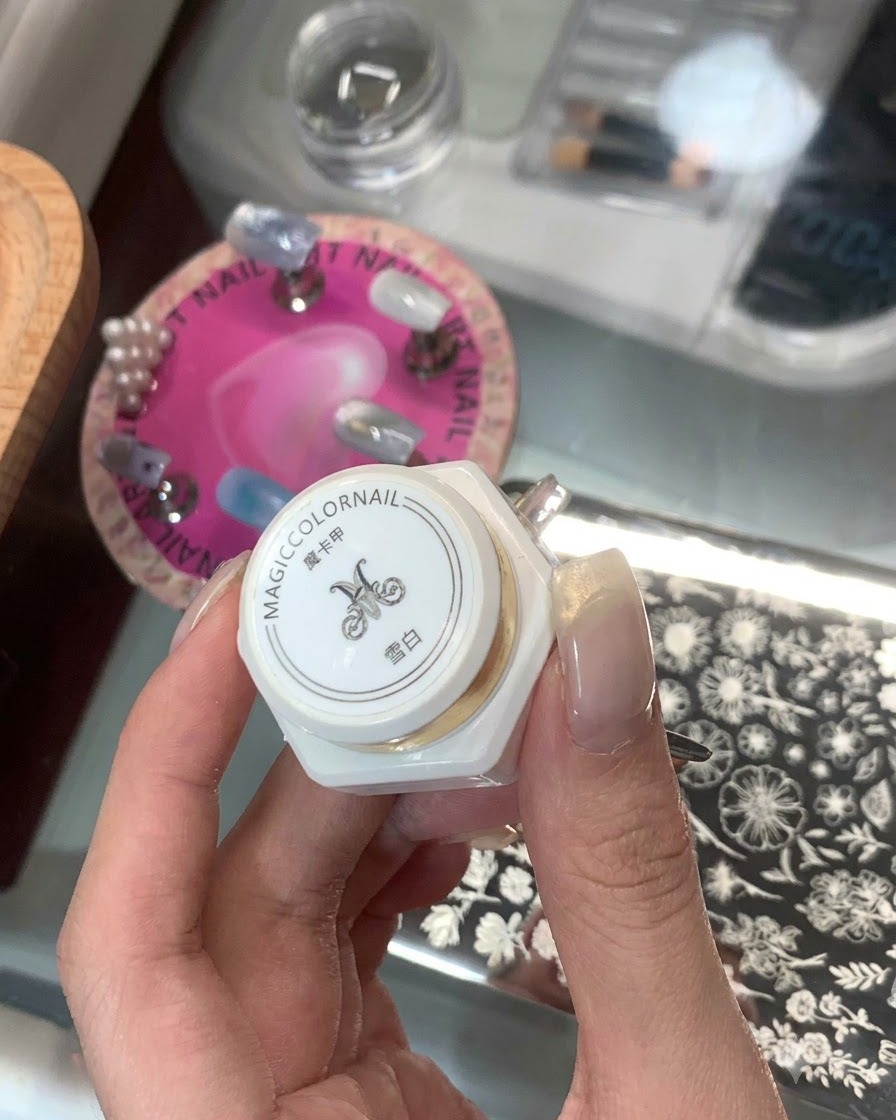 Una mano che regge un prodotto per stamping bianco in flacone con caratteri asiatici e una piastra per stamping sullo sfondo.